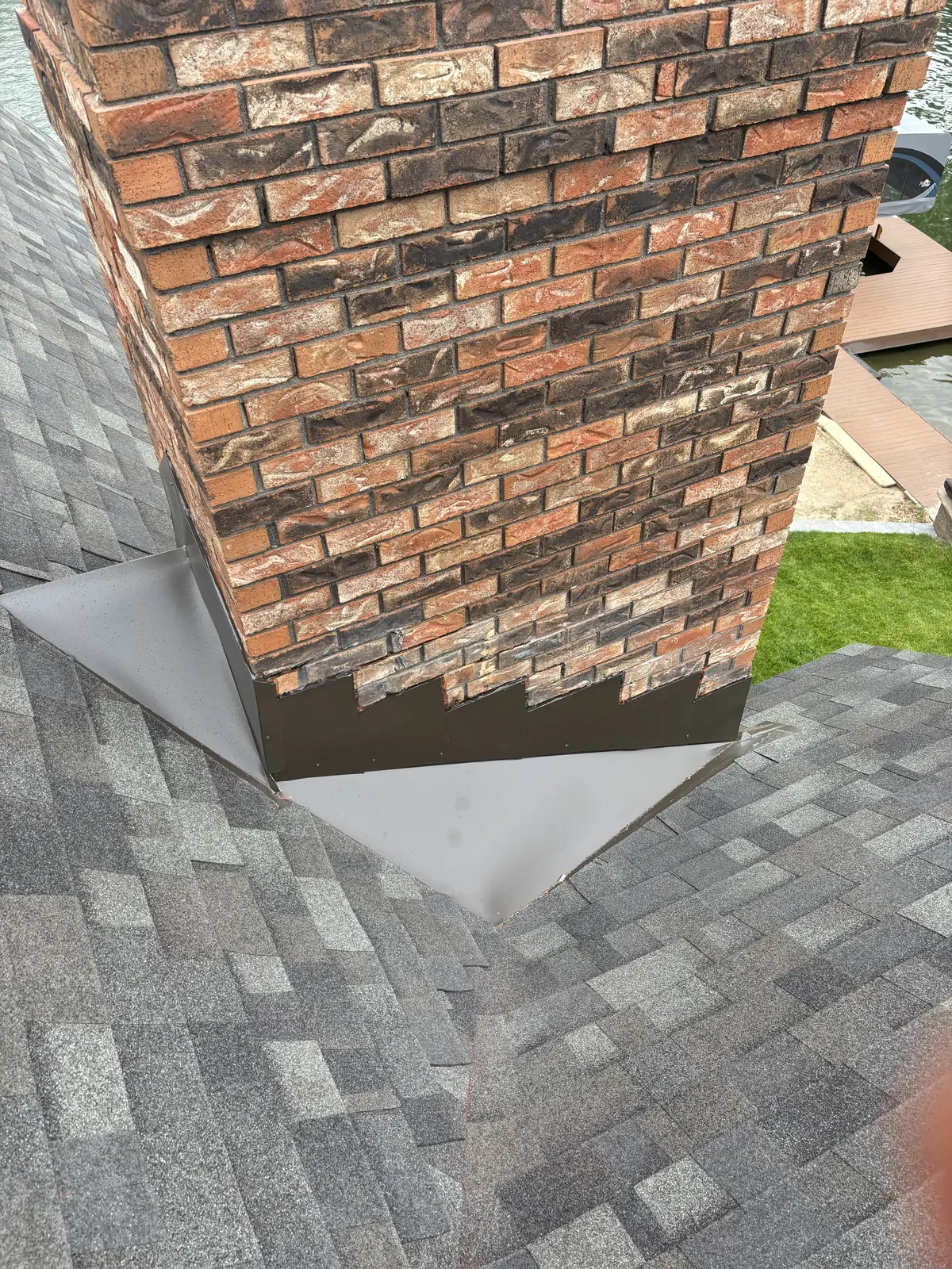 Brick chimney with new dark brown metal flashing on a finished grey shingle roof