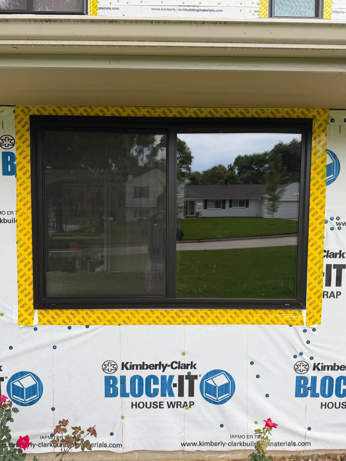 Dark framed sliding window set in an opening taped at the edges, with house wrap across the wall around it