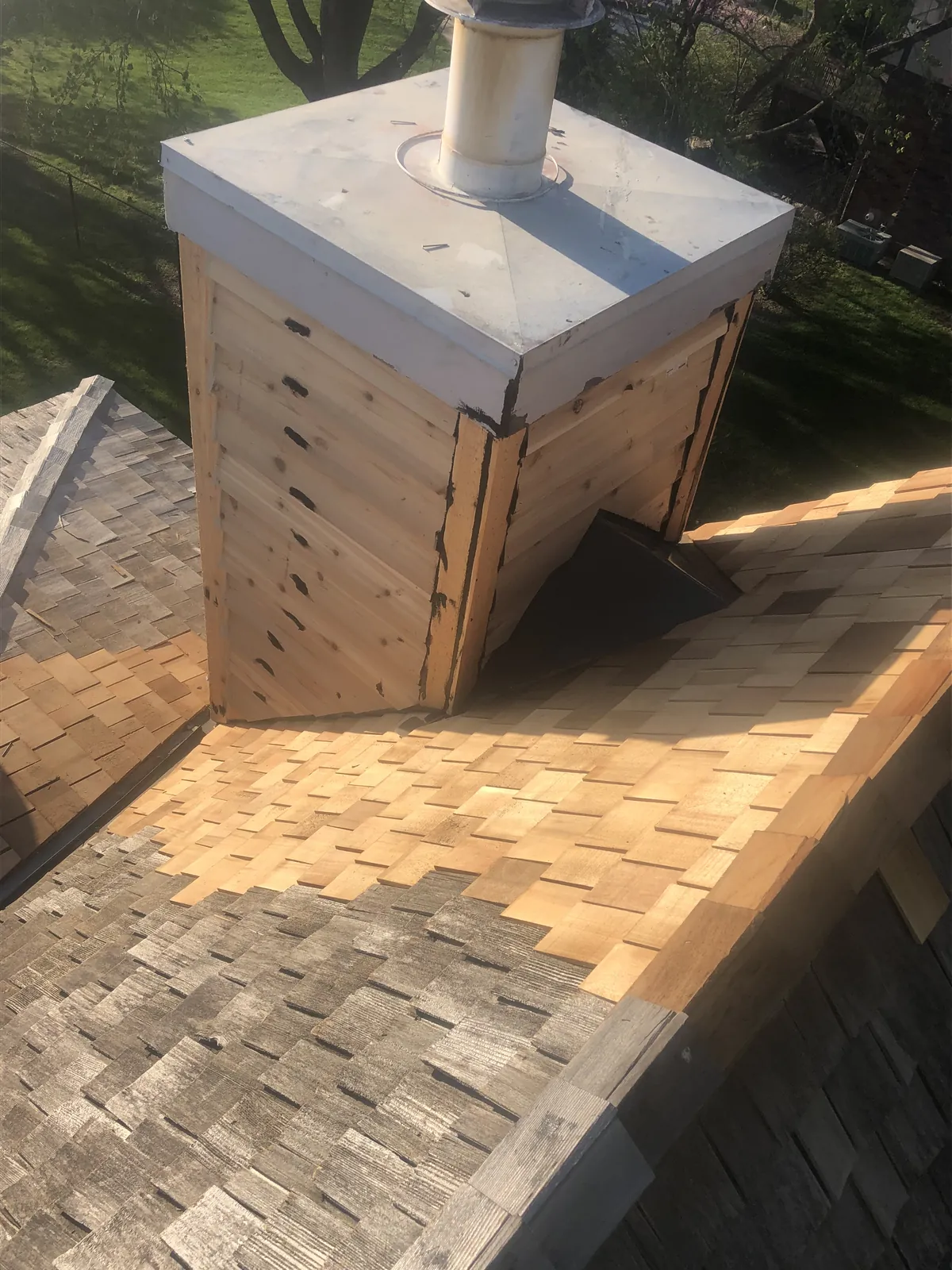 Cedar clad chimney chase with a new metal cap, on a roof part way through a cedar shake reroof
