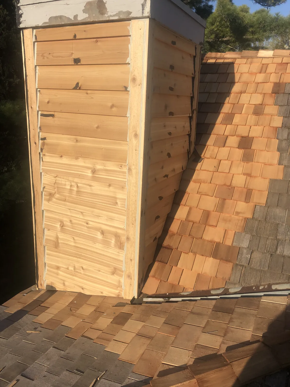 Newly clad cedar chimney chase standing against a new cedar shake roof