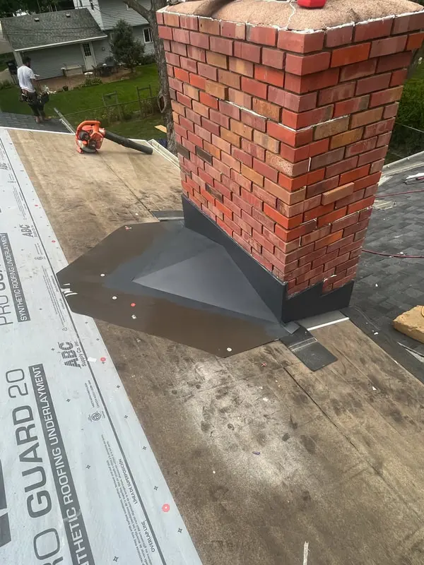 Red brick chimney with new gray step flashing over synthetic underlayment