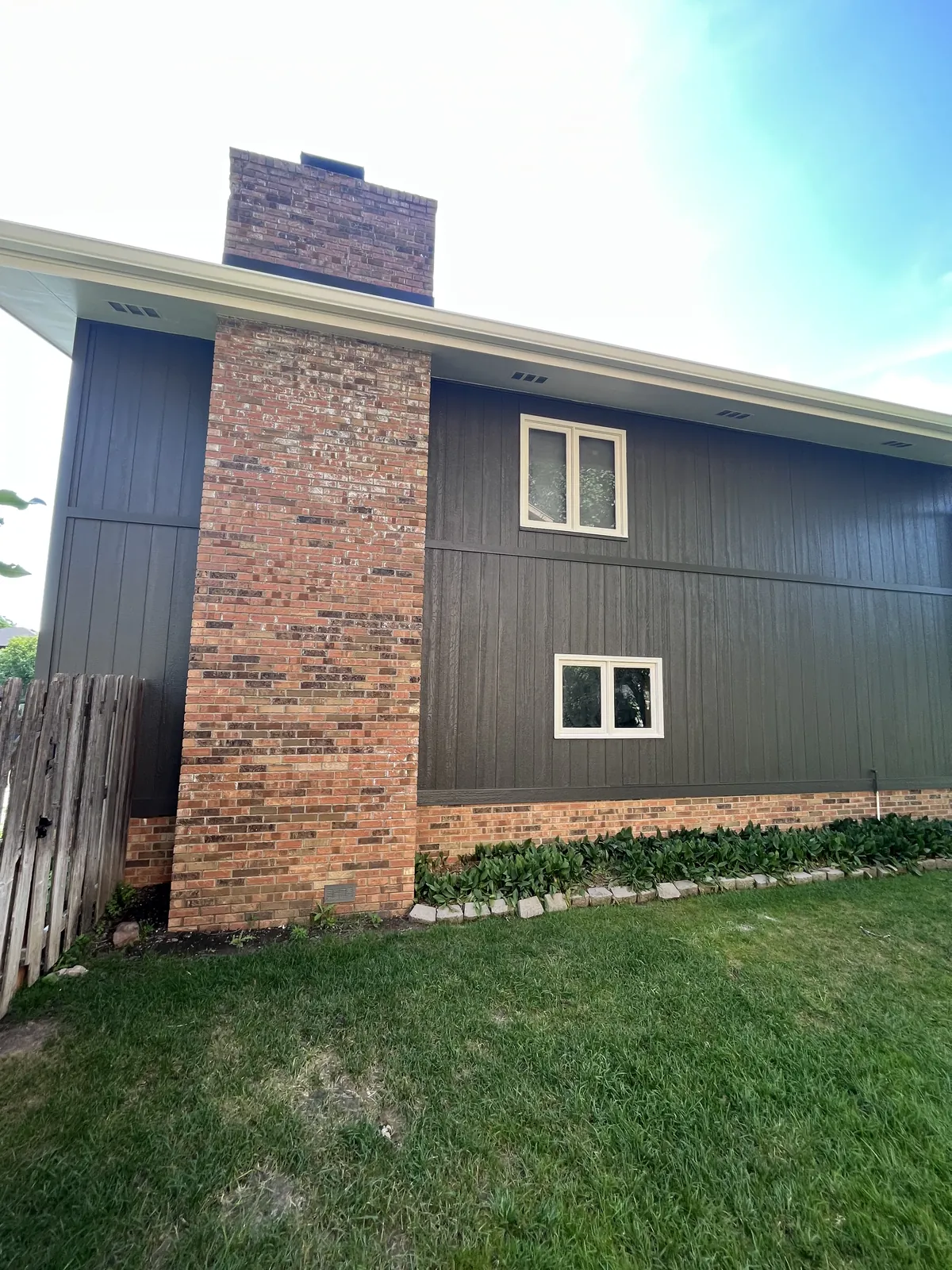 Dark vertical siding finished either side of a tall brick chimney