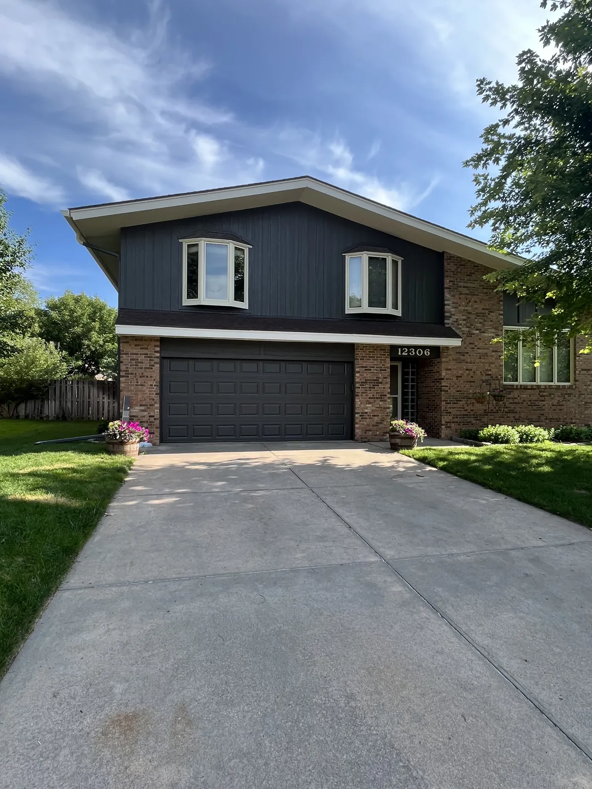 Front elevation of a home finished in dark siding with white window trim and a double garage