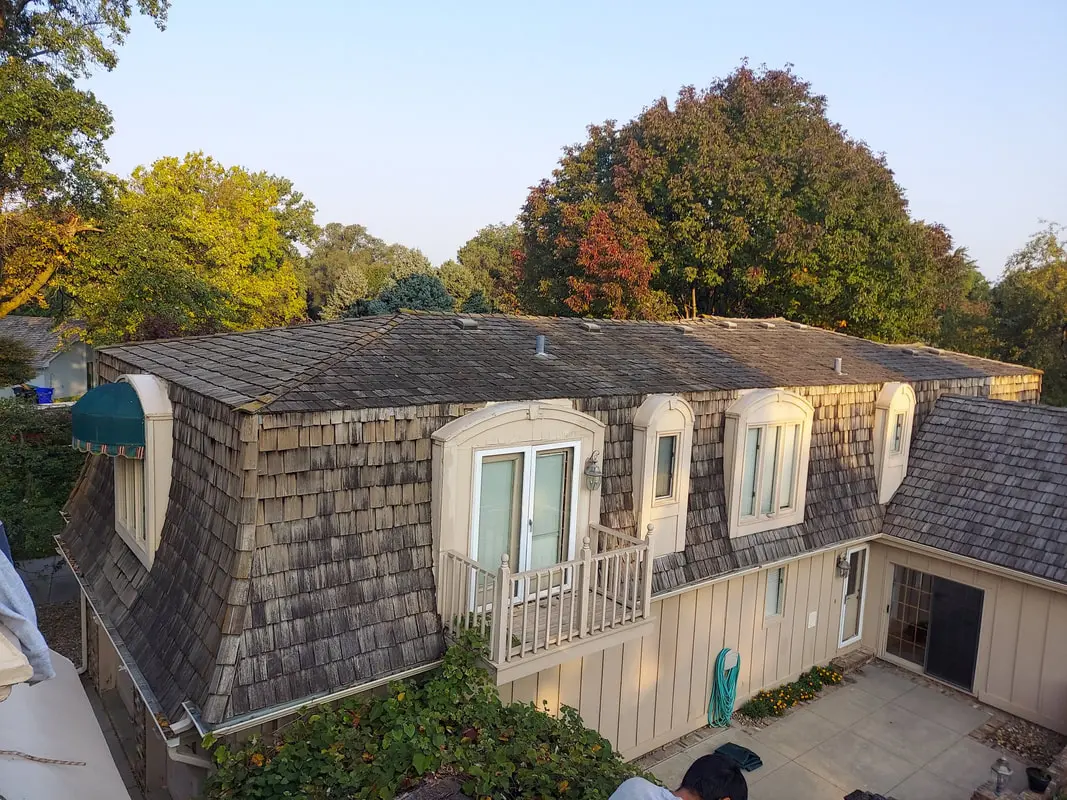 Cedar shake roof and dormers on a house with autumn trees behind it