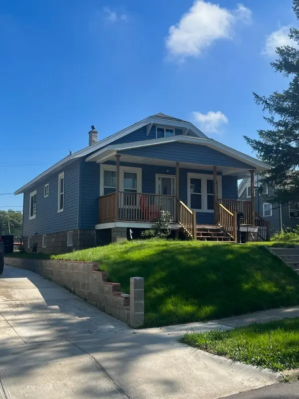 Side elevation of a bungalow with new blue siding and a block retaining wall