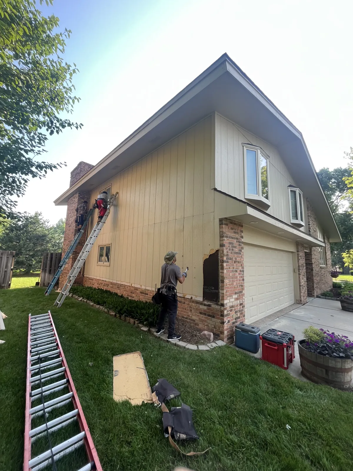 Crew members on ladders tearing old siding off the gable end of a house